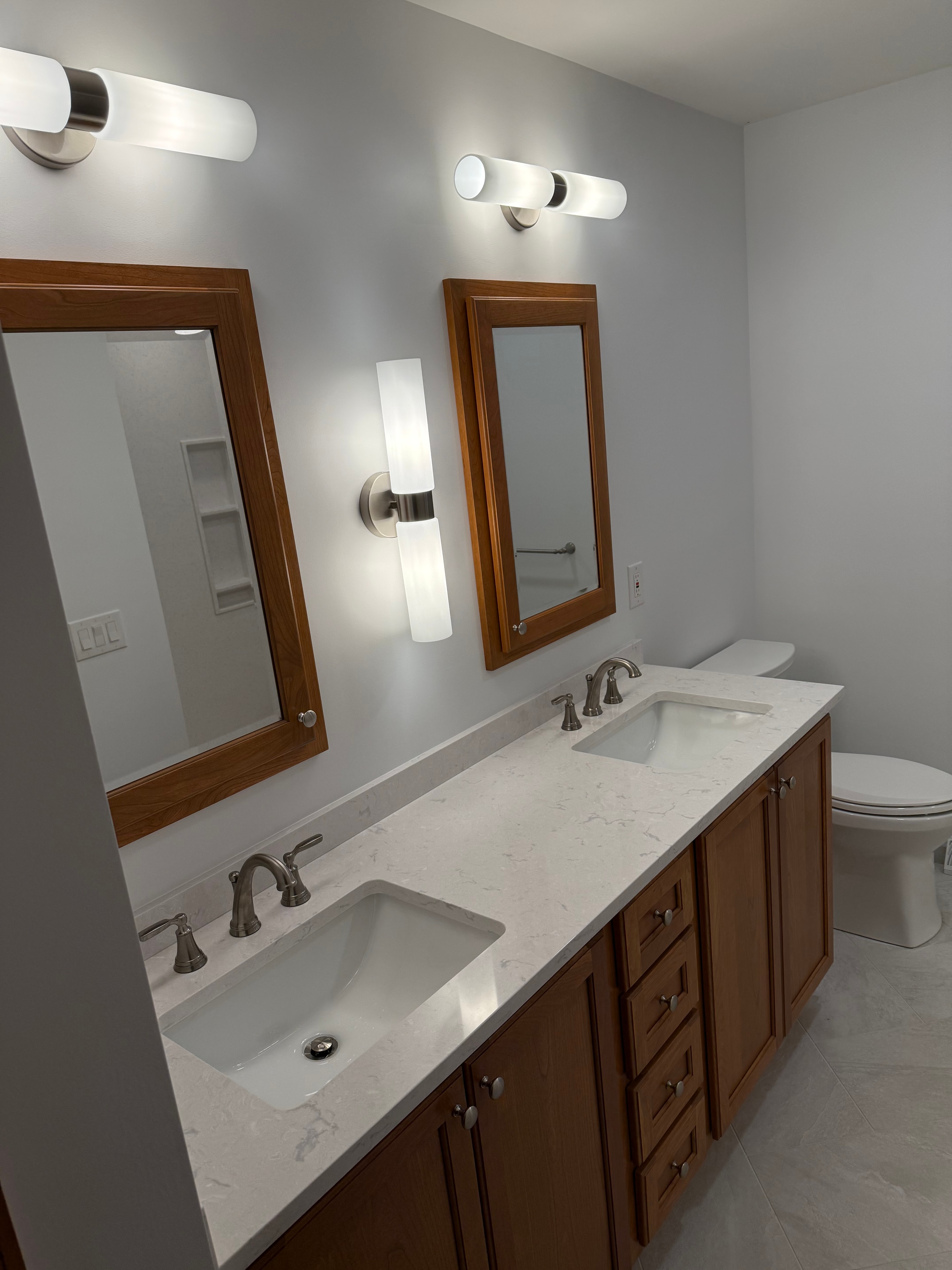 Clifton Park bathroom remodel - dual wood-framed mirrors with brushed nickel sconces and marble quartz countertop