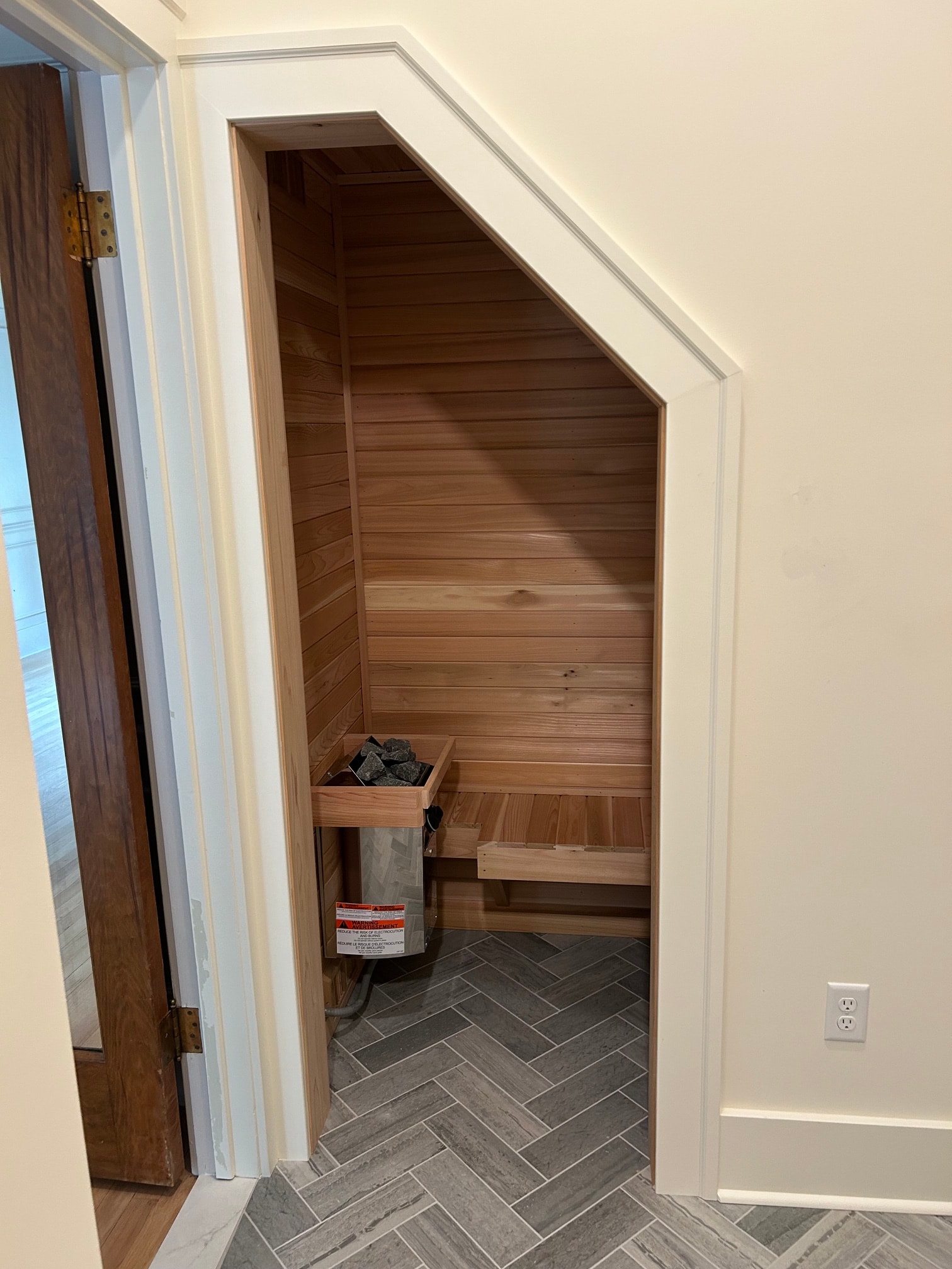 Niskayuna sauna and spa bathroom - cedar sauna entry under staircase with herringbone tile surround and sauna heater inside