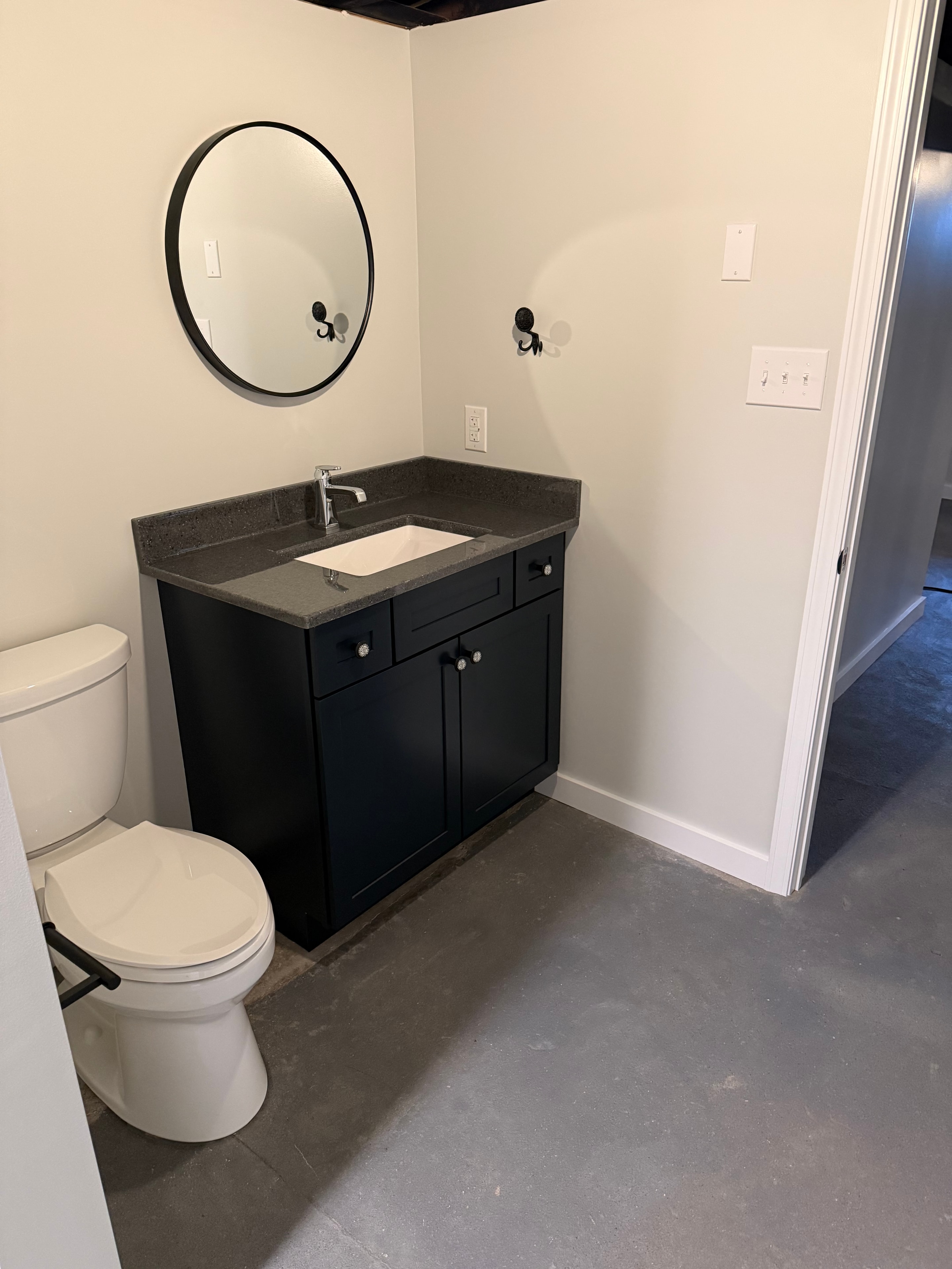 Schuylerville basement bathroom - wide view showing full layout with black vanity, round mirror, toilet, and tub shower unit