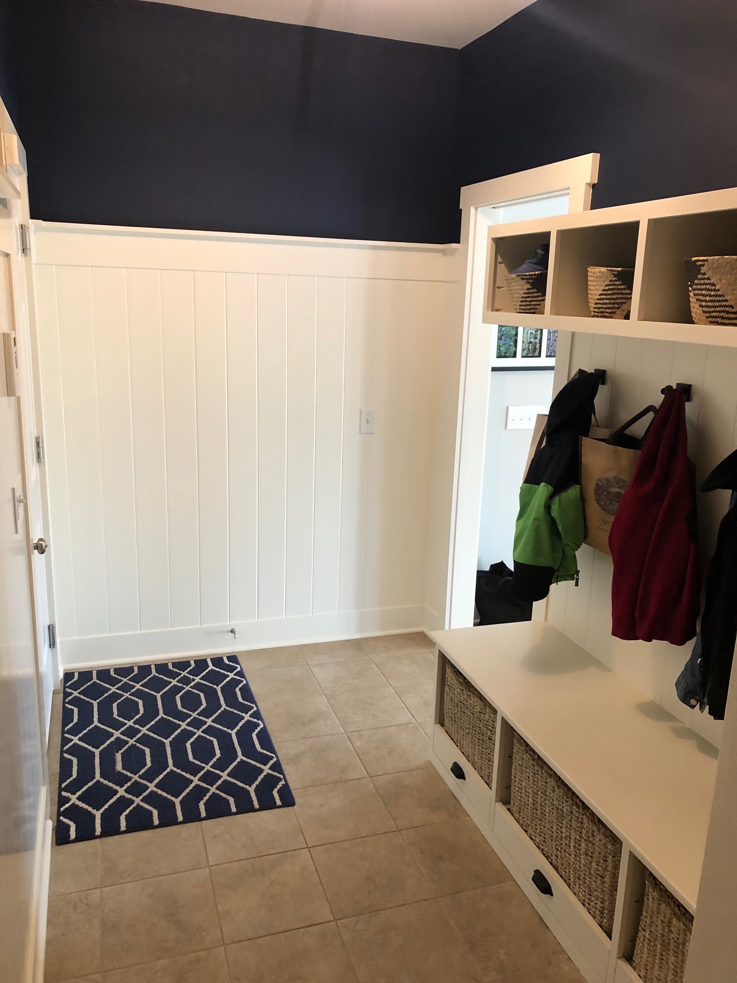 Altamont mudroom full room view with shiplap walls, built-in bench, woven basket cubbies, large format tile floor, and navy geometric rug