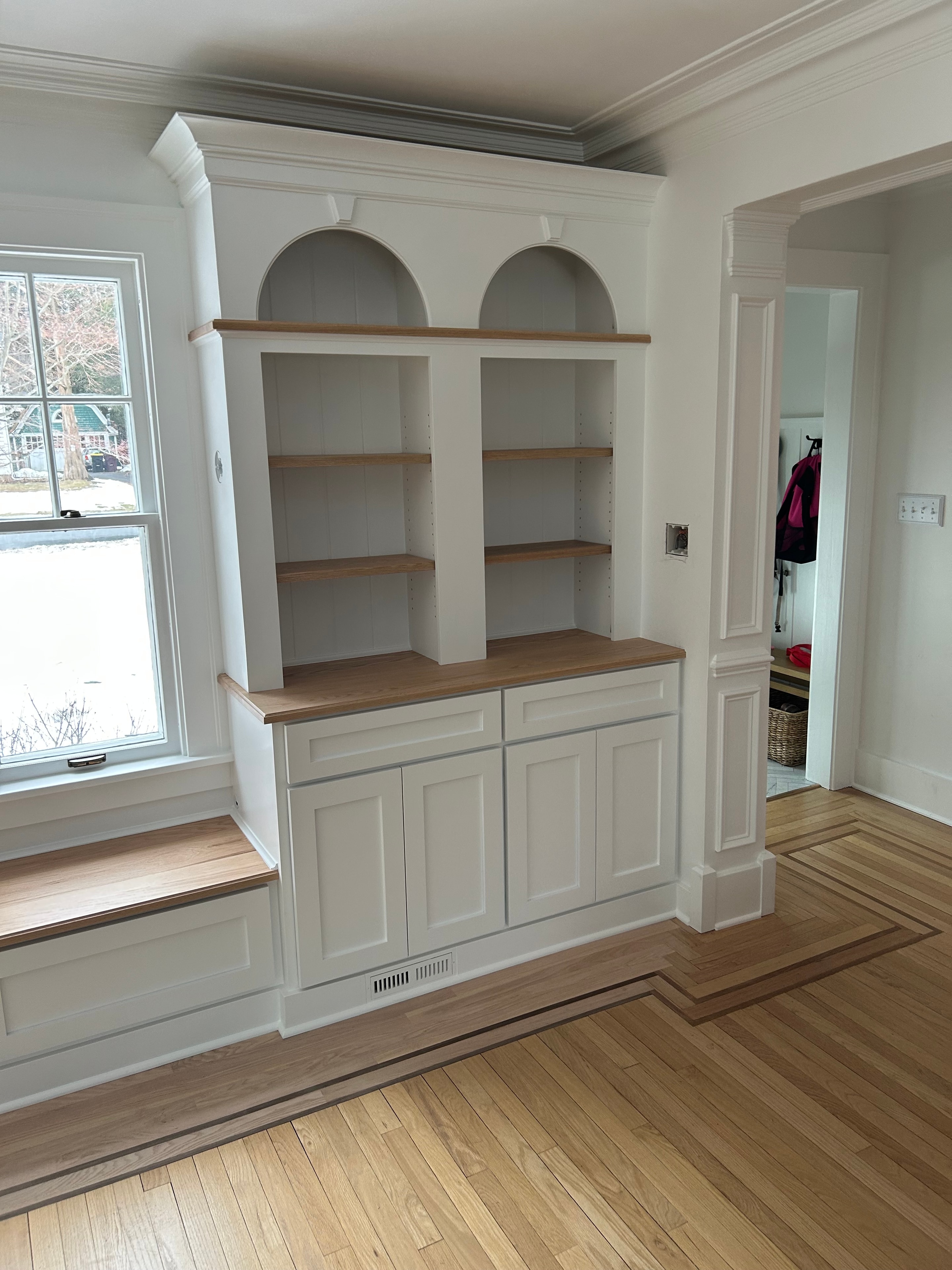 Niskayuna built-in bench - upper bookcase tower detail with arched niche, oak shelving, raised panel lower cabinets, and coffered ceiling