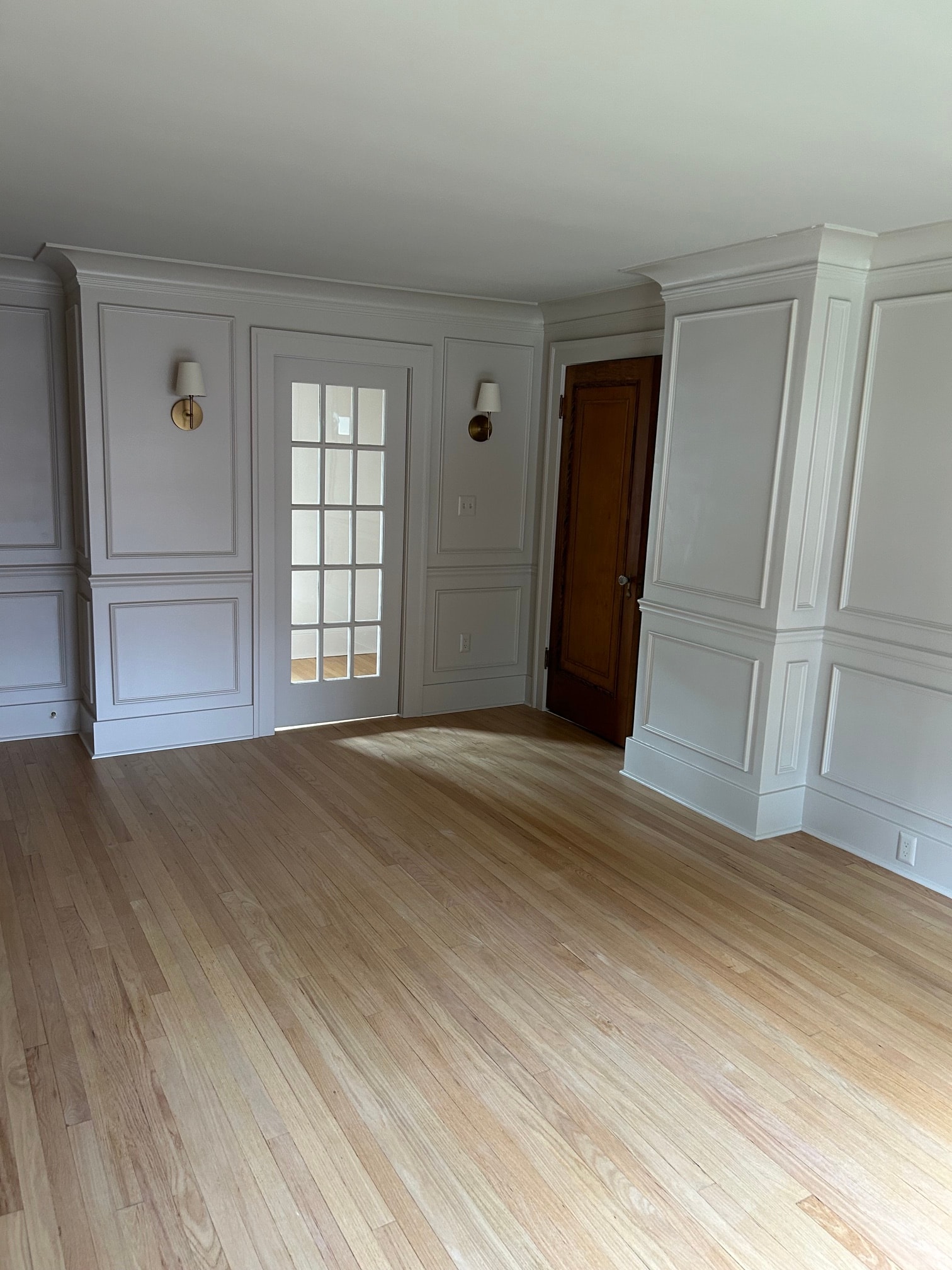 Niskayuna master bedroom custom built-in window surround with grid glass panels, brass sconce lighting, raised panel wainscoting, and coffered ceiling