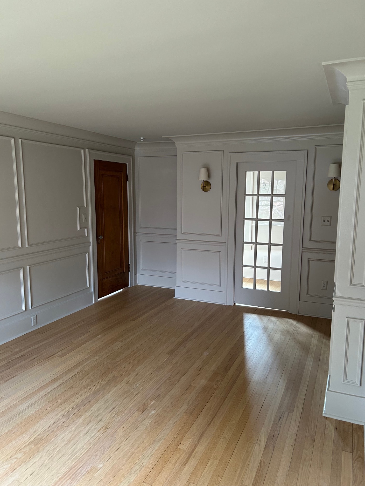 Niskayuna master bedroom full view of built-in window surround with grid glass, brass sconces, raised panel wainscoting, coffered ceiling, and oak hardwood floor
