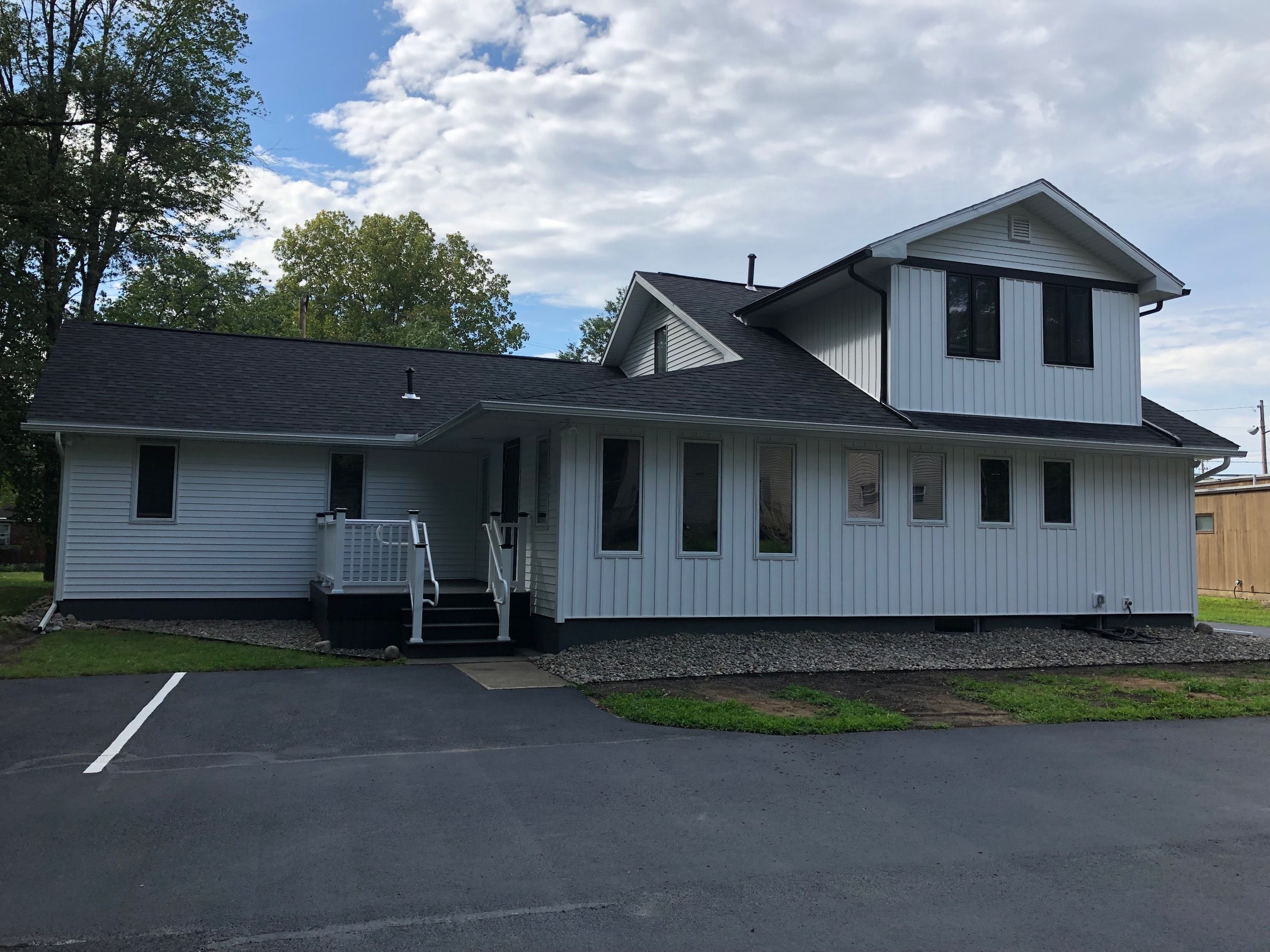 Colonie office remodel during construction showing new white board-and-batten siding, dark trim windows, and accessible entry stairs